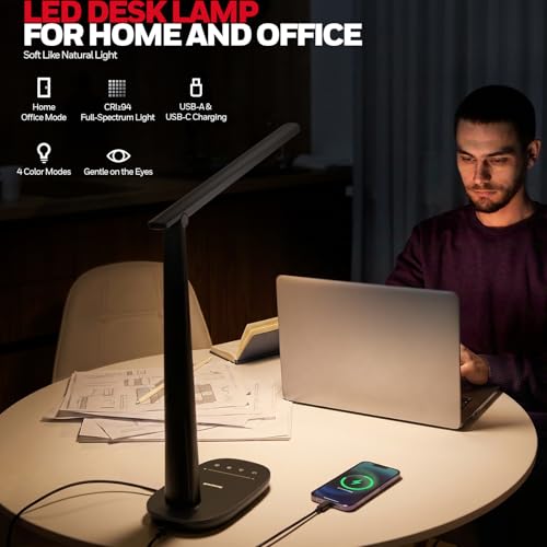 Man working on a laptop at a desk with an LED desk lamp illuminating the area.