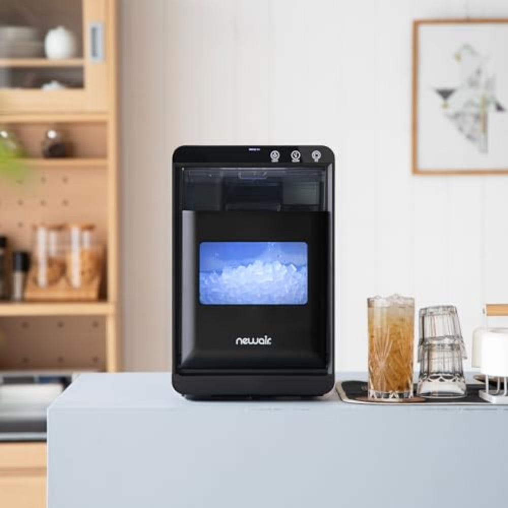 Black Newalk water dispenser on a kitchen counter with a glass of iced drink and a pitcher.