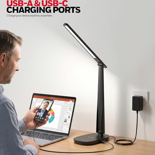 Person using a laptop with a black adjustable desk lamp on a wooden desk.